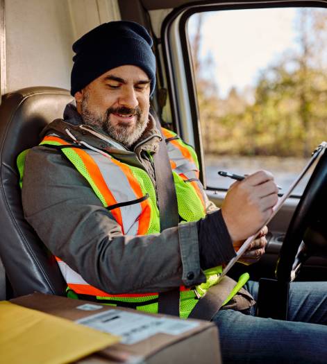 Happy delivery man taking notes while sitting in truck cabin. Truck driver writing on clipboard while preparing for the delivery and sitting in vehicle cabin.